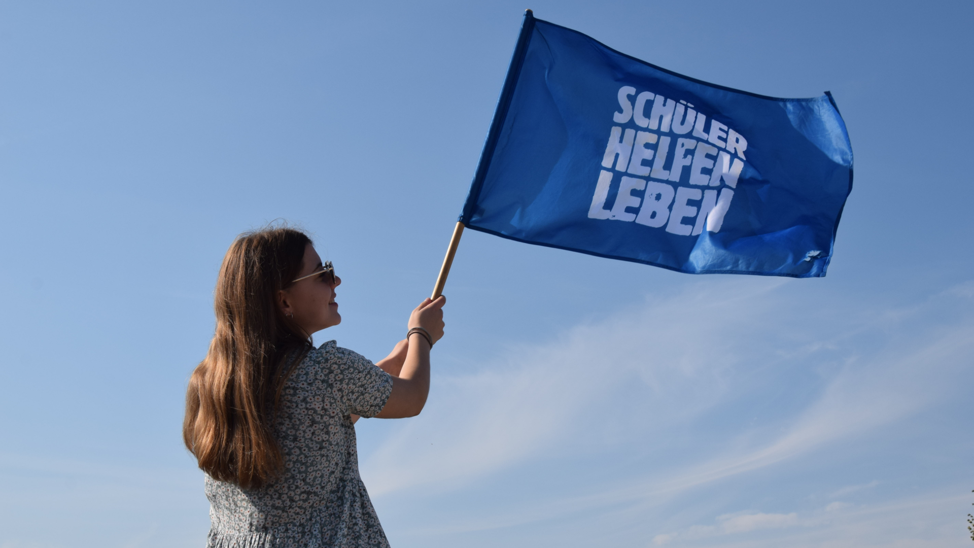 Junges Mädchen schwenkt Fahne mit Schüler Helfen Leben Text vor blauem Himmel