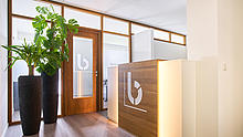 Flur mit grünen Pflanzen sowie einer Tür und einem Empfangstresen, auf denen das burgenta-Logo abgebildet ist.
