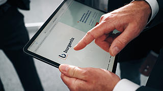 Zwei Hände halten ein Tablet mit der Ansicht der burgenta-Website.
